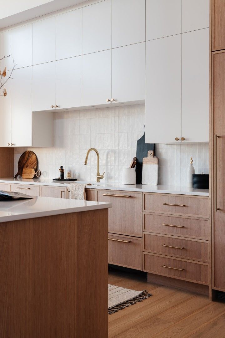 Two-tone slim shaker kitchen with white upper cabinets, warm wood lower cabinets, brass hardware, and modern backsplash.