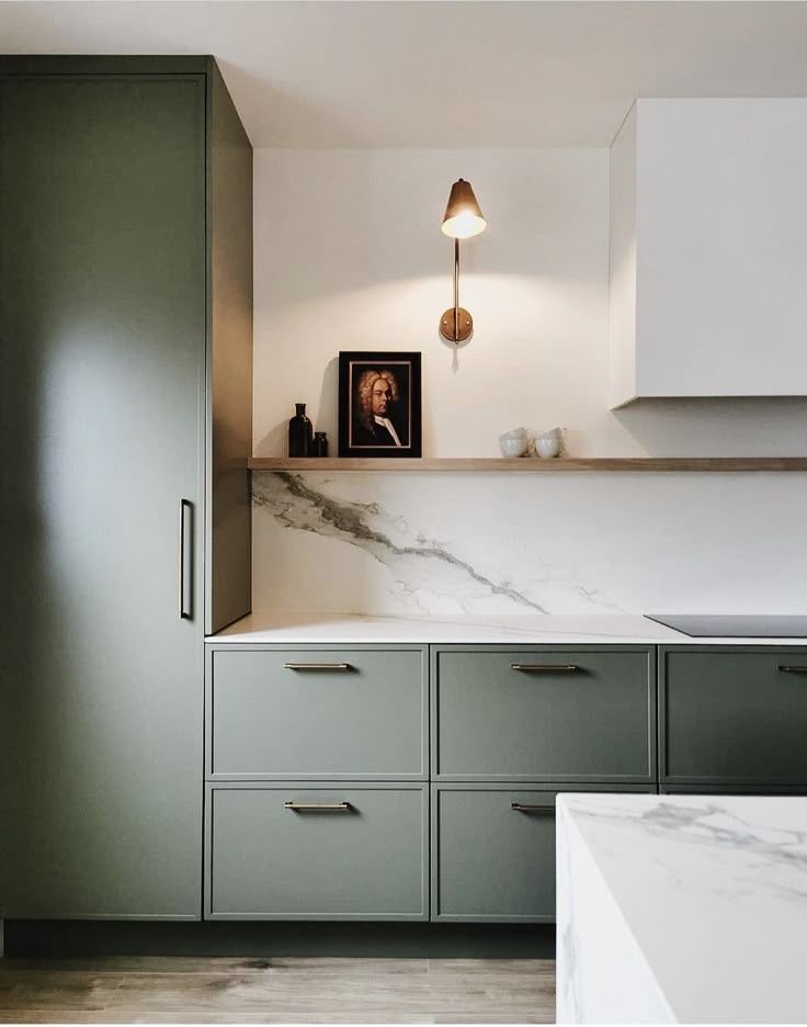 Slim shaker cabinet doors in deep green with modern kitchen design, marble backsplash, and minimalist brass hardware.