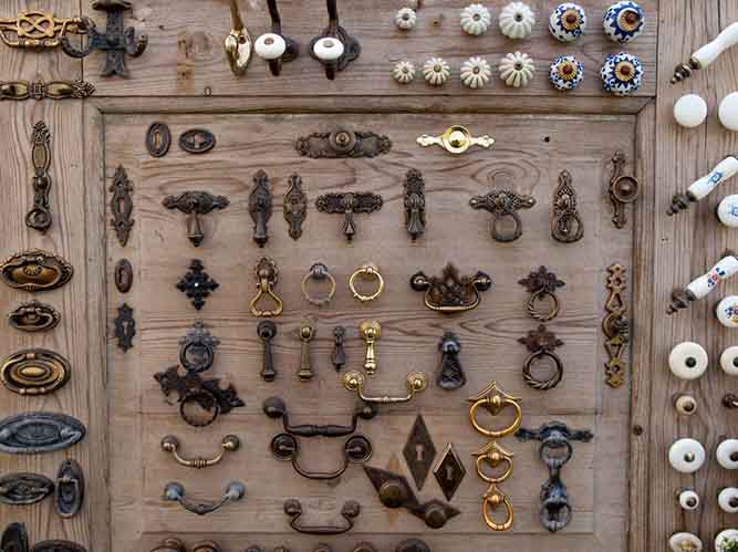 A cabinet door with a variety cabinet pulls and knobs attached.