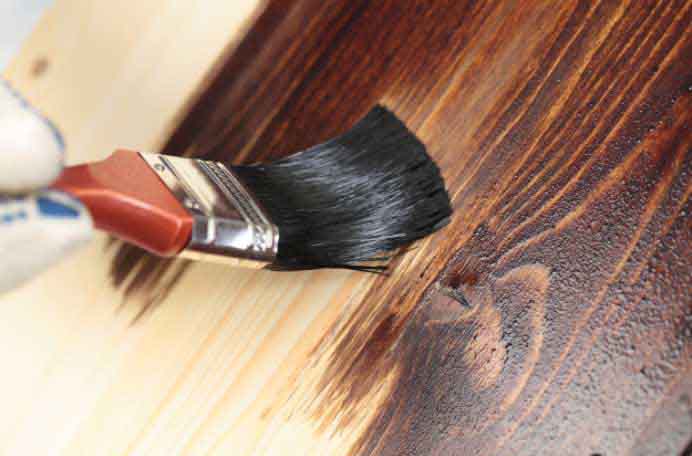 A person brushing stain on wood.