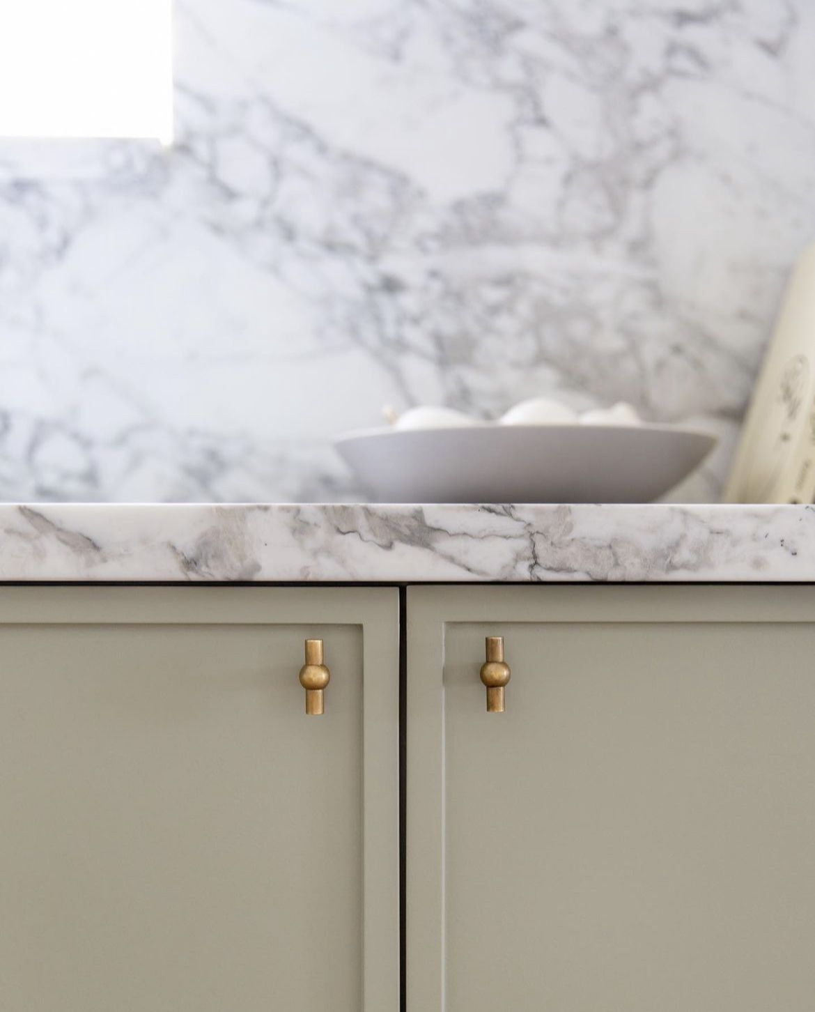 Slim shaker cabinet doors with small brass knobs, marble countertop, and warm neutral kitchen design.