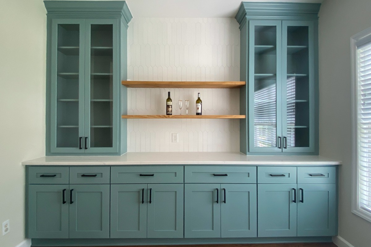 Blue-Green Shaker Cabinet Doors for Custom Built-Ins Blue-green shaker cabinet doors with floating wood shelves and glass-front built-ins in a custom home bar and entertaining space.