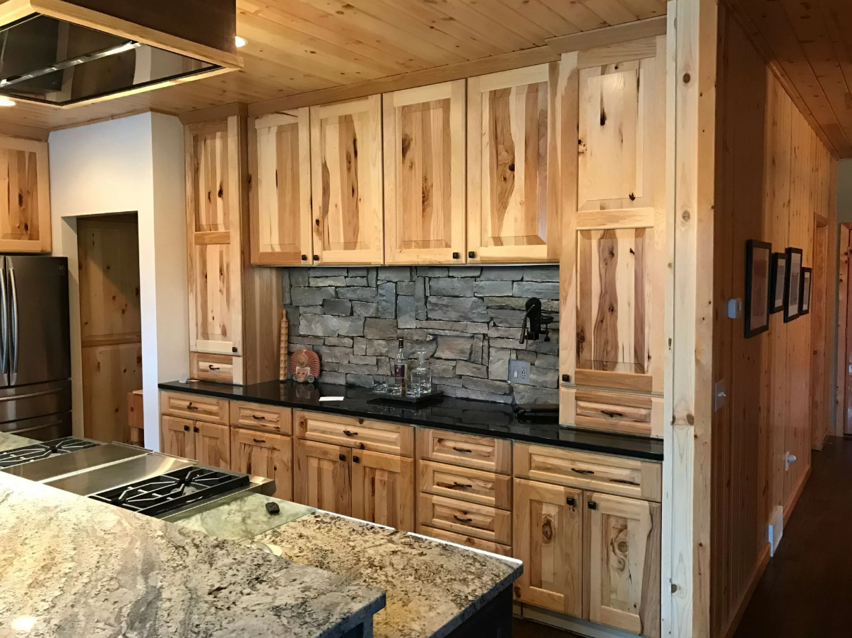 Built-In Rustic Hickory Cabinets with Stacked Stone Backsplash Built-in rustic hickory cabinets with a stacked stone backsplash, black countertops, and floor-to-ceiling storage.