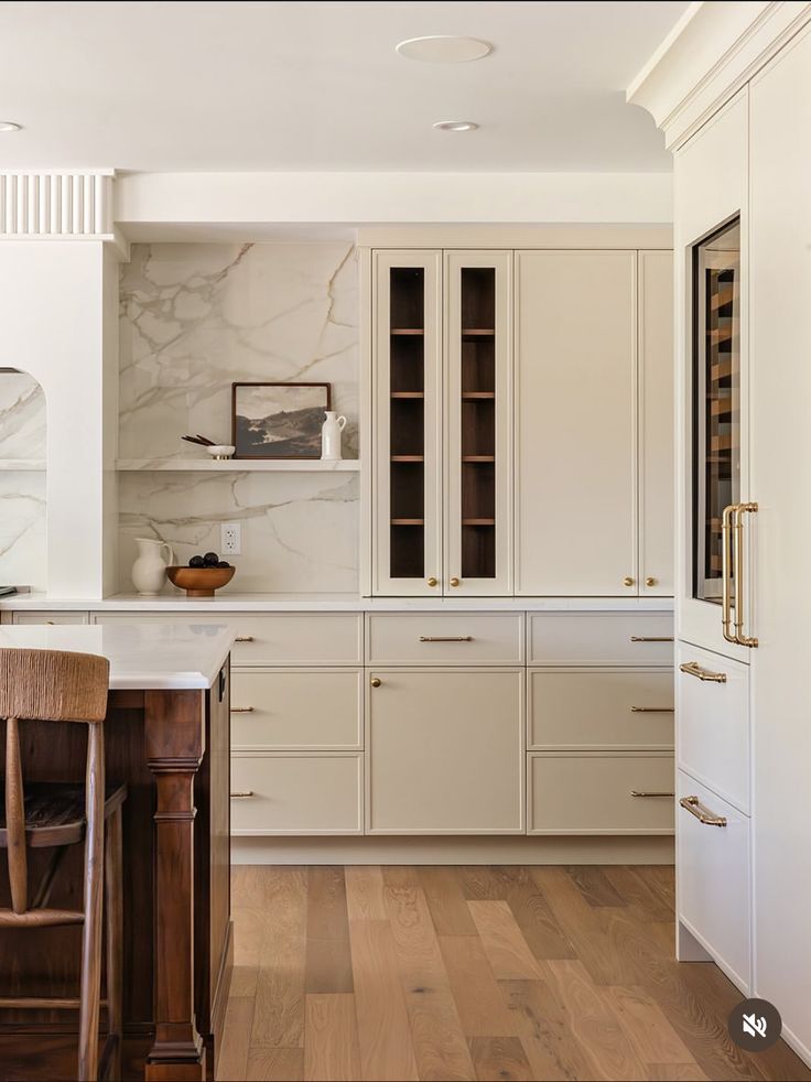 Buttercream slim shaker cabinet doors with brass hardware, glass panel uppers, and marble backsplash in a warm kitchen.