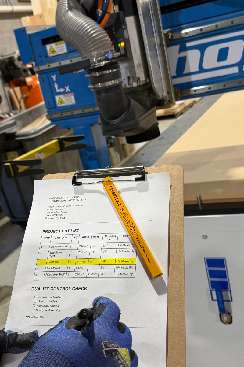 Employee verifying a custom cabinet cut list at a CNC machine before manufacturing made-to-spec cabinet components.
