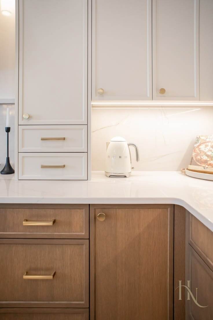 Slim shaker cabinet doors in a warm wood finish paired with white upper cabinets and brass hardware in a modern kitchen.