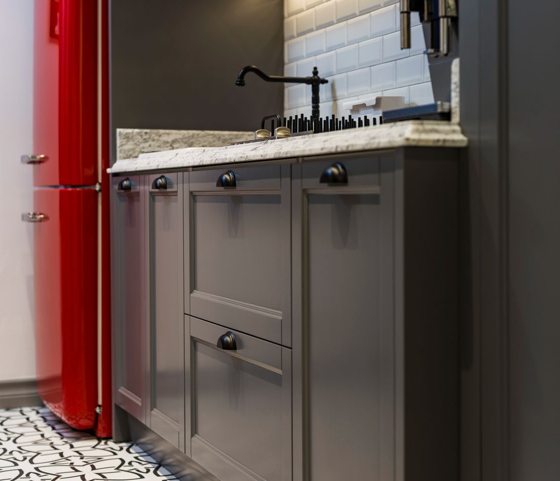 A kitchen with a red refrigerator and gray cabinets. 