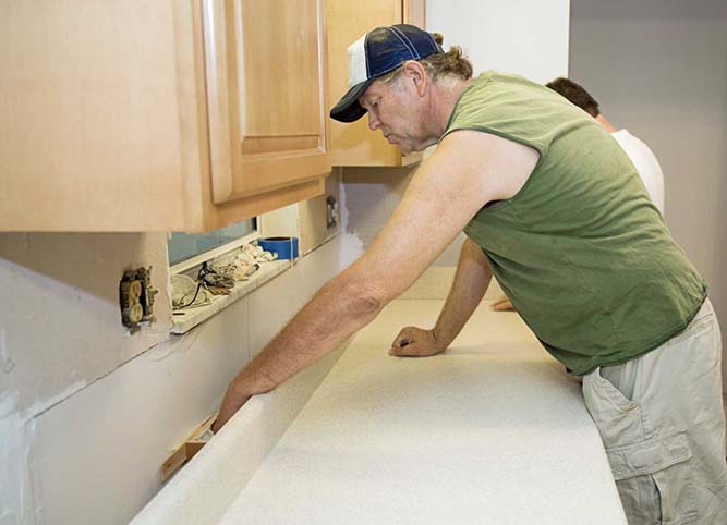 A person installing a countertop onto a base cabinet box.