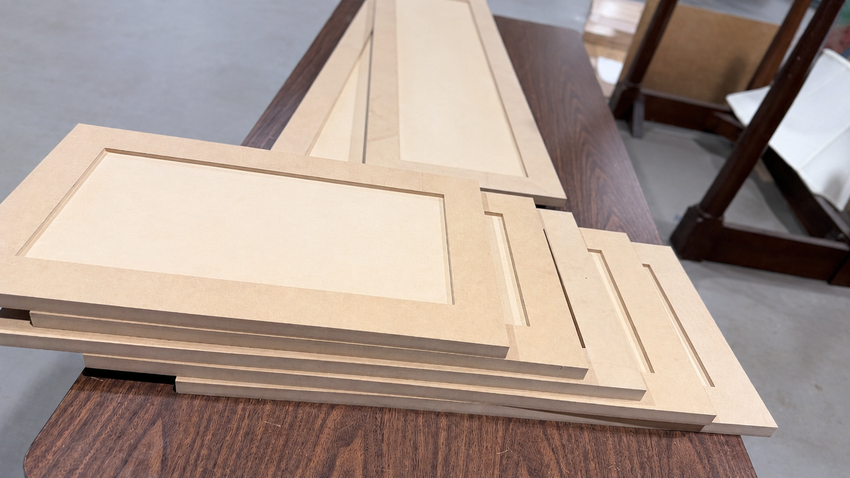 Woodworking workshop with cabinet panels Unfinished MDF shaker cabinet doors and drawer fronts stacked on a worktable in a woodworking shop.