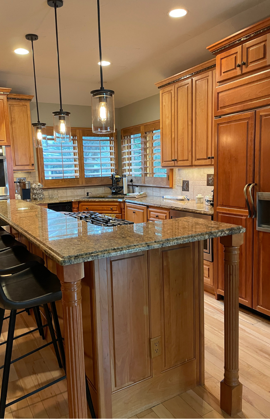 Before photo of a traditional oak kitchen with large island, raised panel cabinet doors, granite countertops, and decorative wood details prior to DIY cabinet door replacement and a modern Shaker kitchen update.