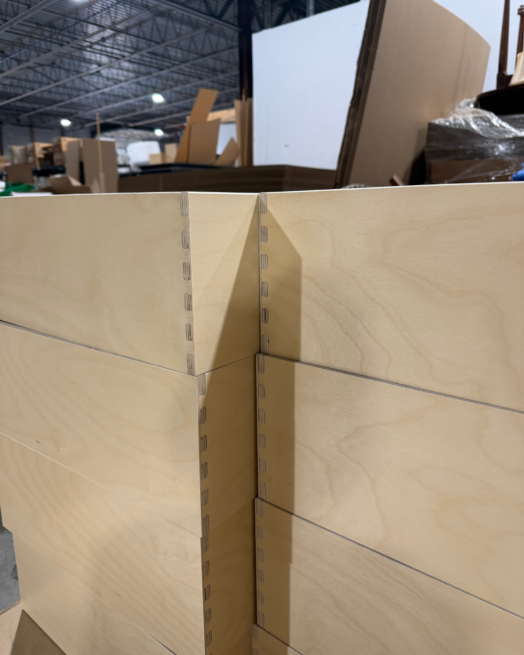Stacked pre-finished 9-ply birch drawer boxes with dovetail construction in a cabinet manufacturing facility.