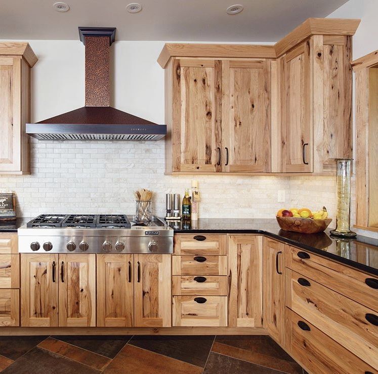 Rustic Hickory Kitchen Cabinets with Natural Wood Grain Rustic hickory kitchen cabinets with natural knots, black hardware, light stone backsplash, and a metal range hood.