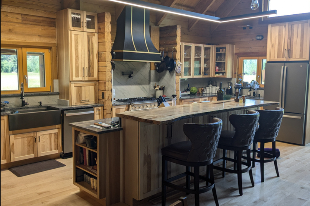 Rustic Hickory Kitchen Cabinets with Black Accents Rustic hickory kitchen cabinets with a black range hood, black farmhouse sink, large island, and exposed wood beams in a lodge-style kitchen.