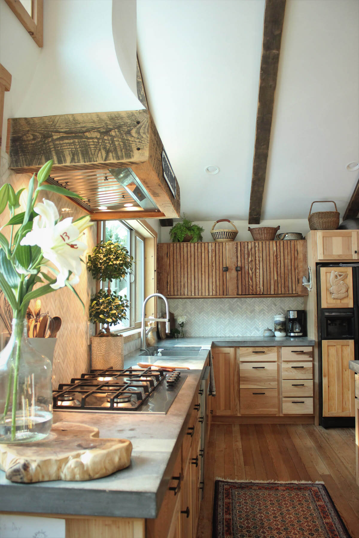 Rustic Hickory Kitchen Cabinets with Vertical Slat Doors Rustic hickory kitchen cabinets with vertical slat cabinet doors, exposed wood beams, a custom wood range hood, and stone countertops.