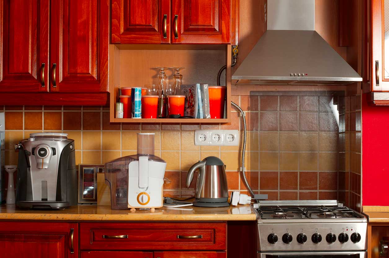 A kitchen with red cabinets, orange and yellow tile backsplash and appliances.
