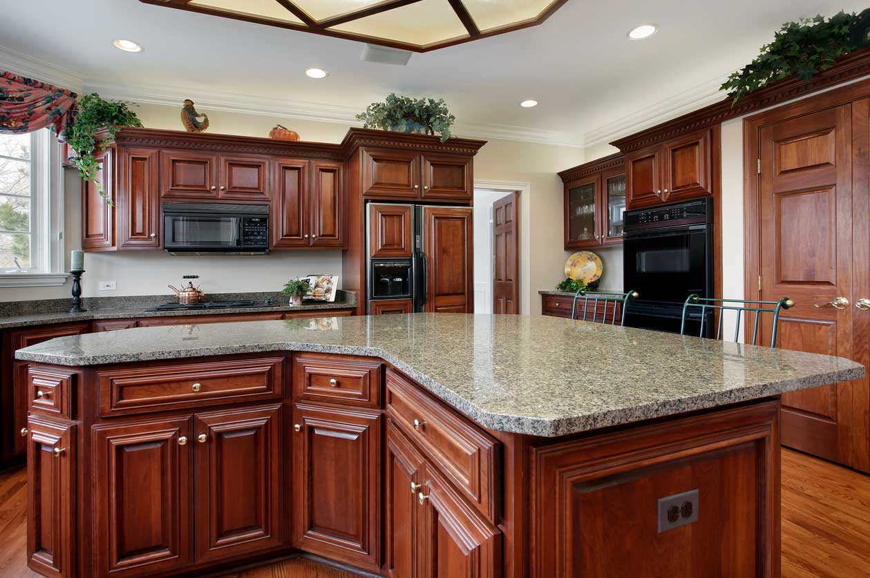 A kitchen with dark stained wood cabinets and a V-shaped center island.
