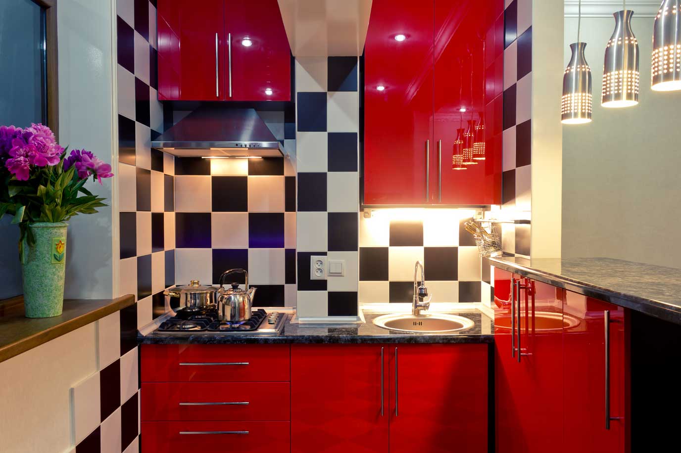 A small kitchen with black and white tile and red cabinets.