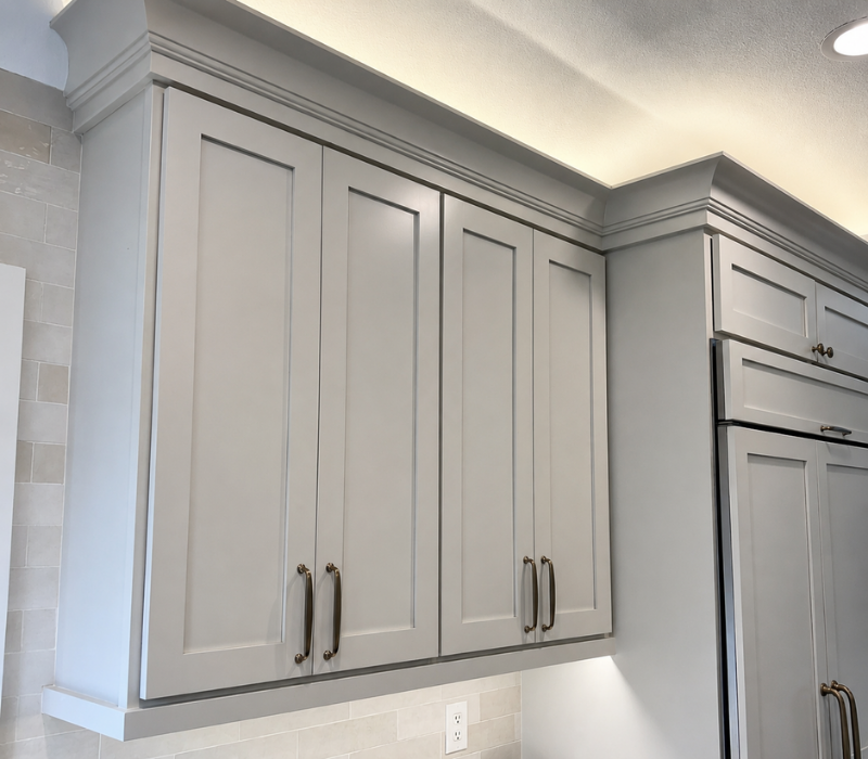 Close-up of soft greige Shaker replacement cabinet doors with upper cabinet lighting and crown molding in a modern kitchen remodel